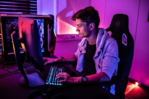 Spieler sitzt im violett beleuchteten Gaming-Setup vor Monitor und Tastatur