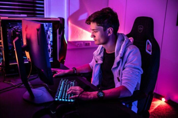 Spieler sitzt im violett beleuchteten Gaming-Setup vor Monitor und Tastatur